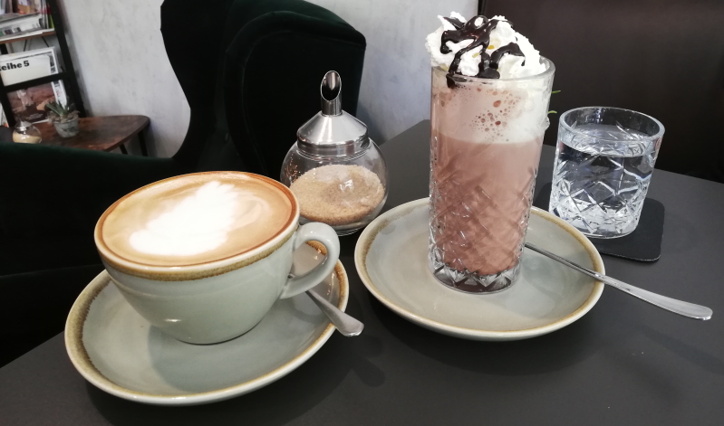 Kaffeespezialitäten werden im Café & Bar deer mit einem Glas Wasser serviert.